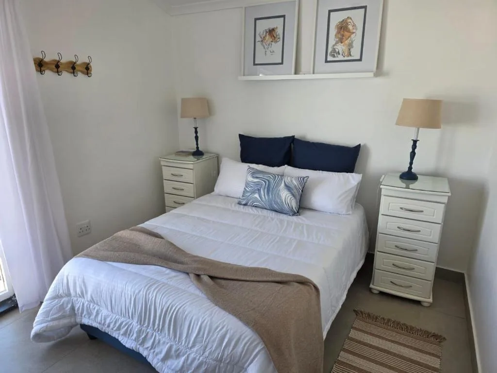 Neatly made bed with white linens and navy pillows in bright bedroom