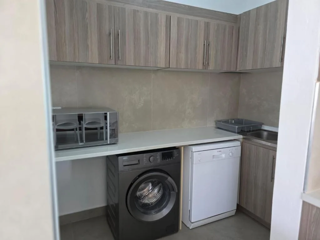 Modern kitchen with wood cabinetry, washing machine, dishwasher, and white countertops