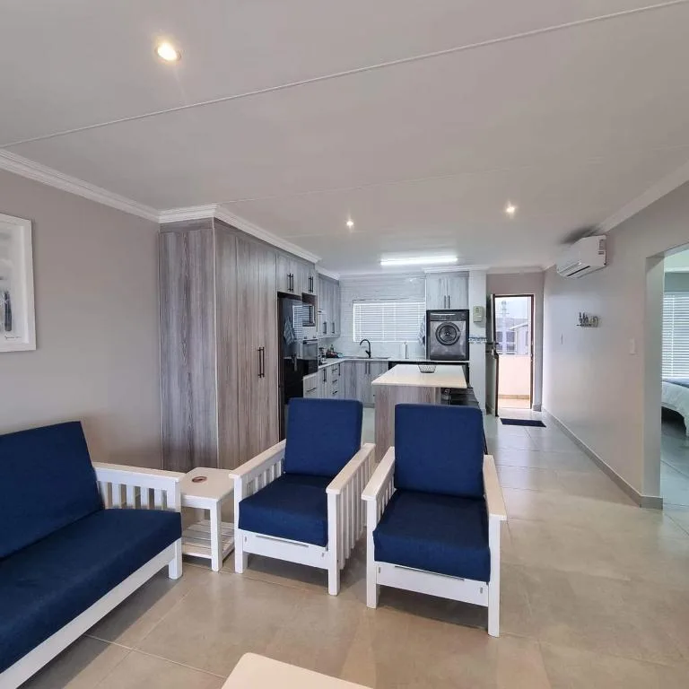 Open-plan lounge with blue upholstered chairs and kitchen area visible