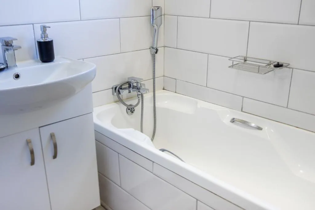 Clean bathroom with white subway tiled walls, vanity sink, and bathtub with shower
