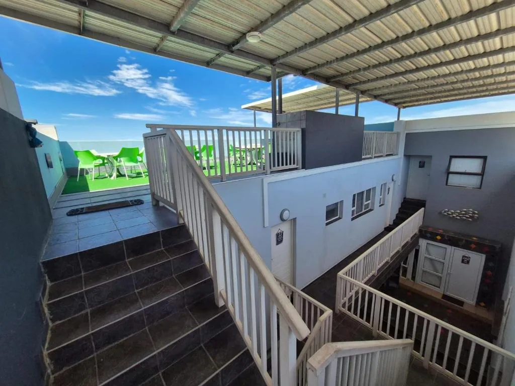 Covered deck with white railings overlooking green beach loungers and ocean