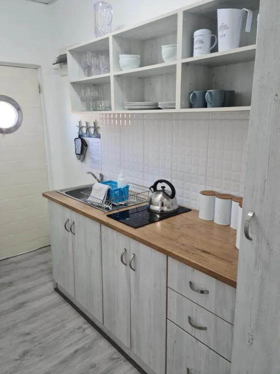 Modern kitchenette with white cabinetry, wooden countertop, and open shelving displaying dishware