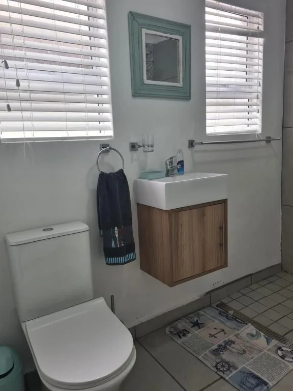 Clean bathroom with white toilet, wooden vanity sink, and bright shuttered windows