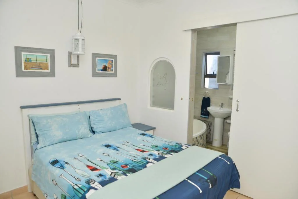 Bright bedroom with queen bed, coastal-themed bedding, and ensuite bathroom
