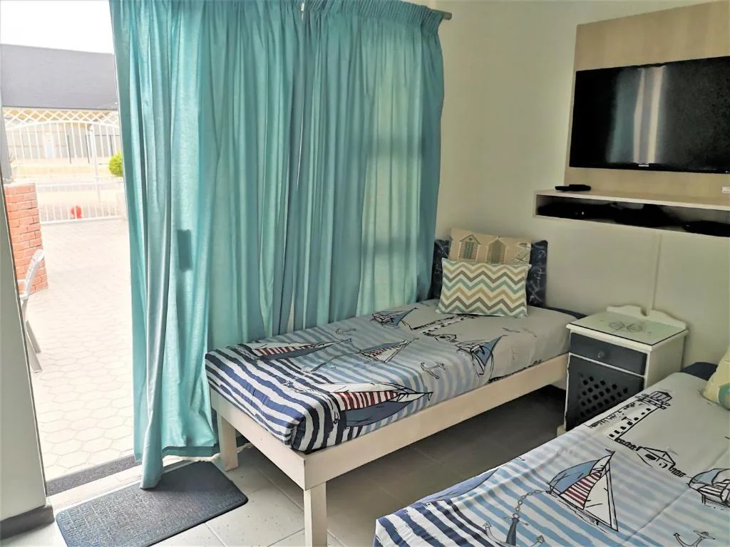 Bright bedroom with single bed, turquoise curtains, and flat-screen TV