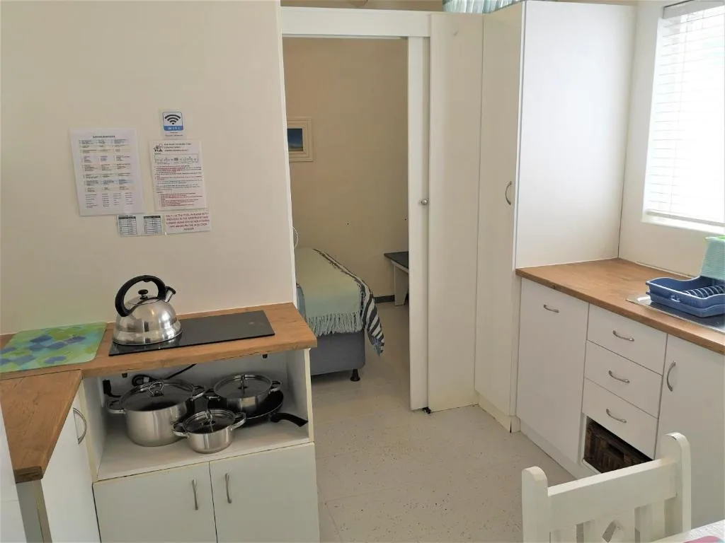 Compact kitchen with stove, cookware, cabinets, and instruction notices on wall