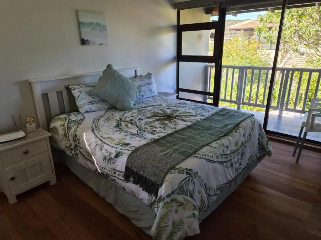 Bright bedroom with patterned bedding, white nightstand, and glass doors opening to deck