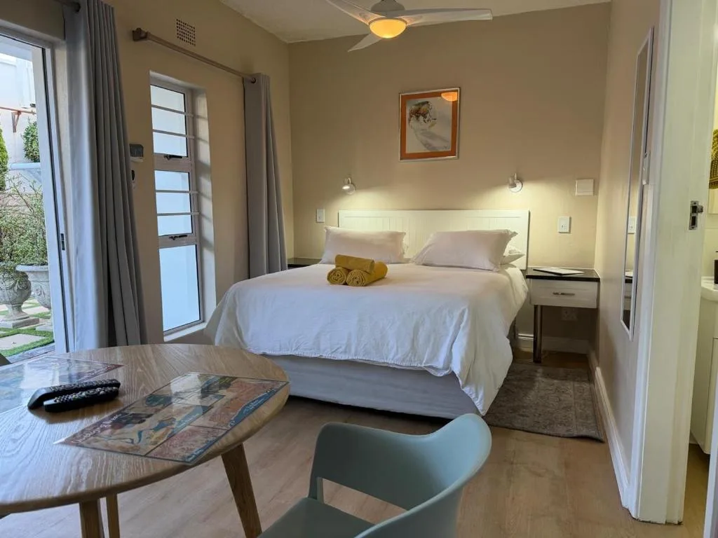 Modern bedroom with queen bed, desk area, and garden view through doors