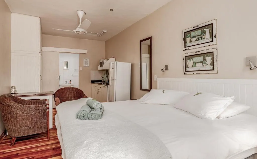 Spacious bedroom with double bed, white pillows, wicker chairs, kitchenette and wall art