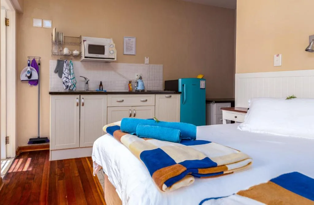 Studio bedroom with twin beds, kitchenette, and wooden flooring throughout