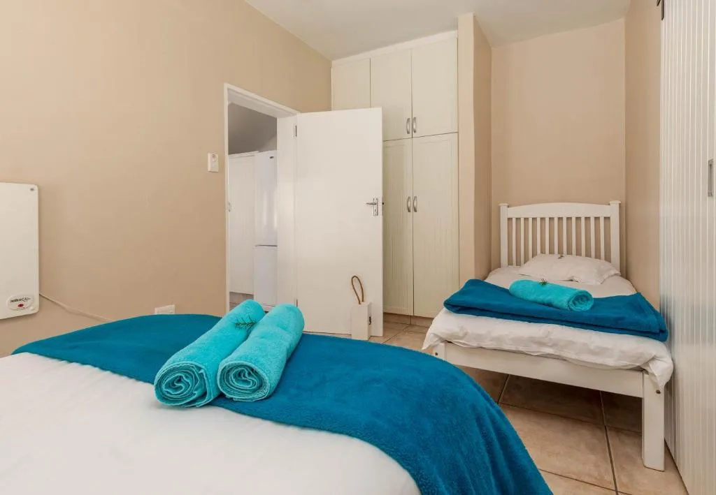 Bright bedroom with two single beds, rolled towels, and built-in wardrobes