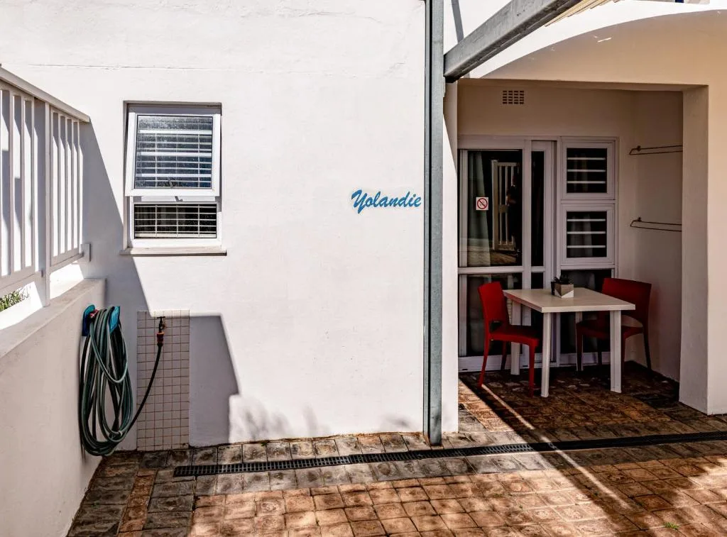 Covered patio area with small dining table and red chairs, garden hose stored on wall