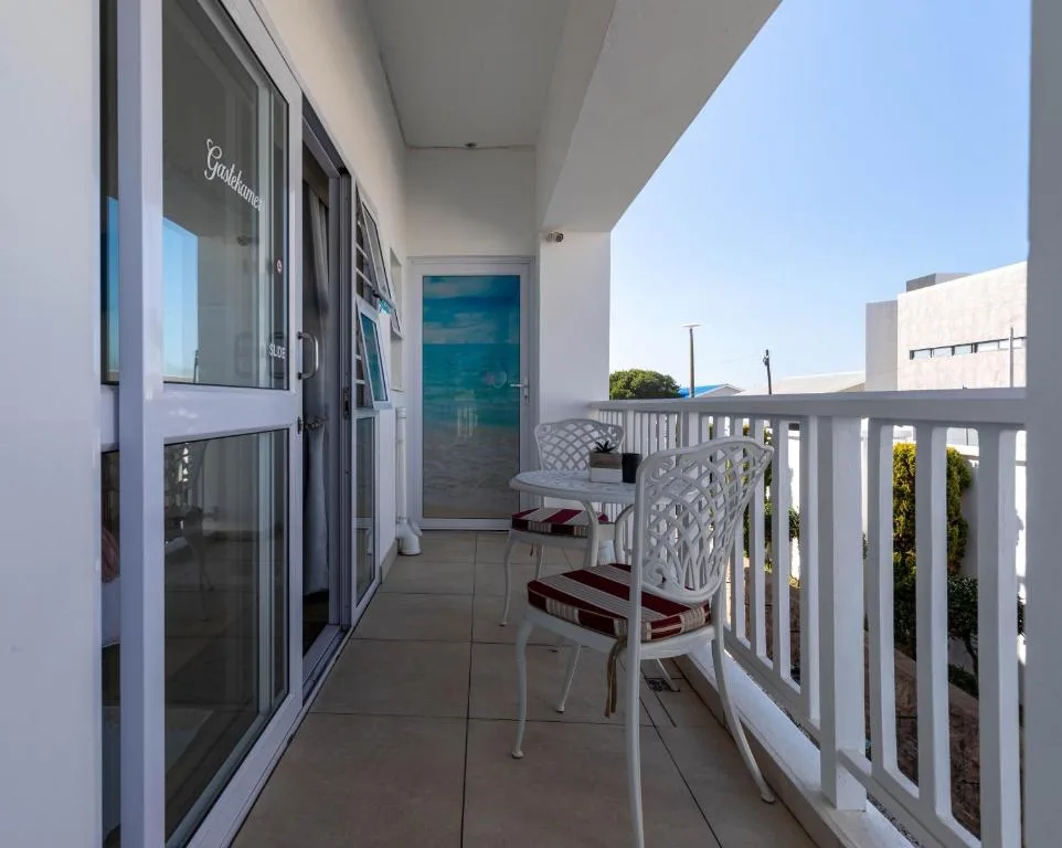Modern balcony with white railings, seating chairs, and ocean view door