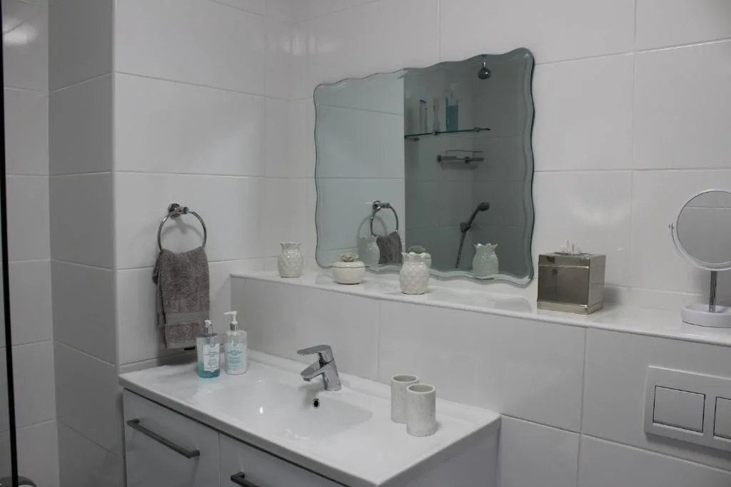 Modern bathroom with white tiles, double vanity, and contemporary wavy mirror