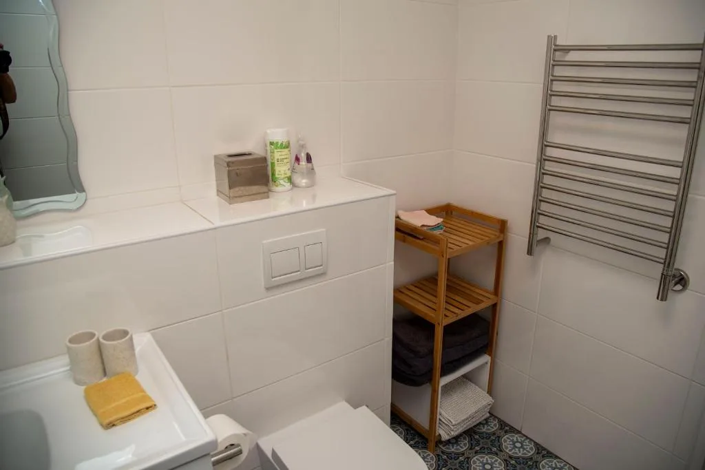 Clean modern bathroom with white tiles, vanity, heated towel rail, and wooden storage