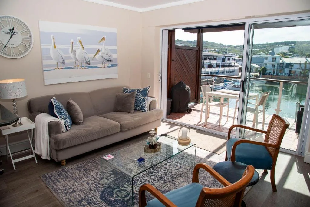 Bright lounge with gray sofa, wooden chairs, and waterfront views through glass doors
