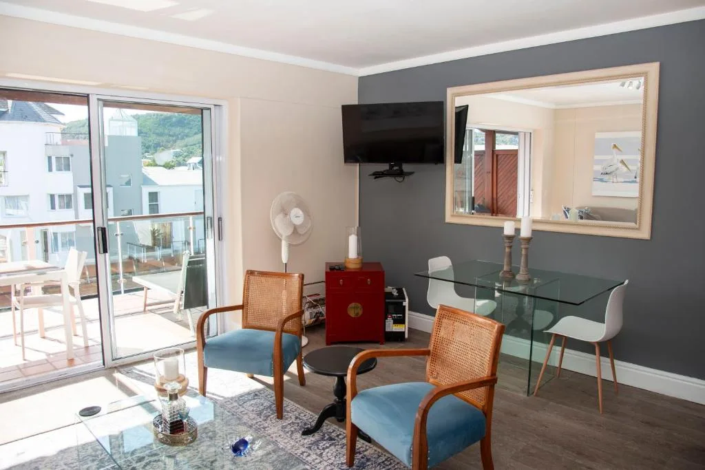 Modern lounge with blue chairs, TV, glass desk, and waterfront views