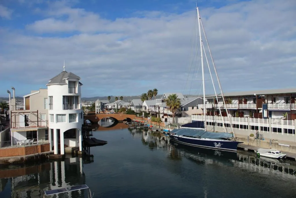 Waterfront canal view with sailboat, modern architecture, and palm trees