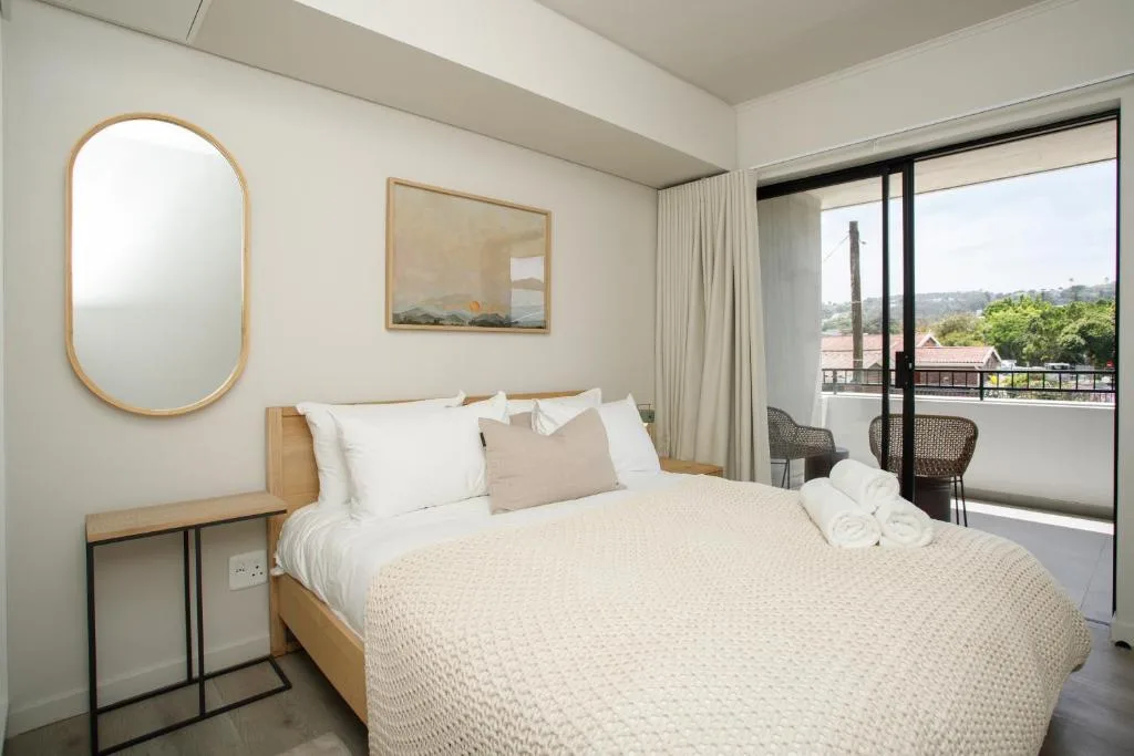 Modern bedroom with queen bed, wooden frame, and scenic balcony view