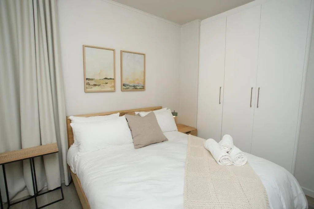 Clean modern bedroom with wooden bed, white linens, and built-in wardrobes