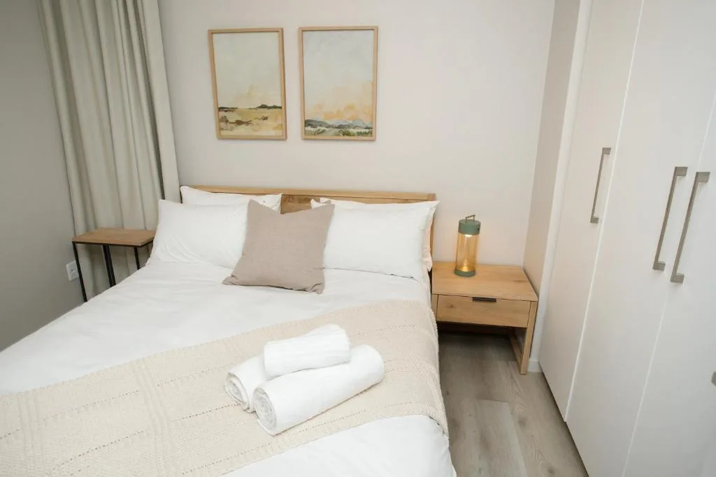 Bright bedroom with queen bed, wooden nightstand, and framed landscape artwork