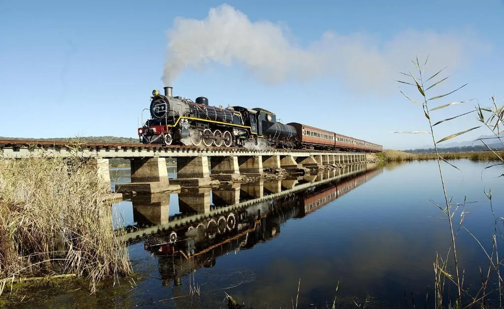 Vintage steam train crossing bridge over calm reflective water