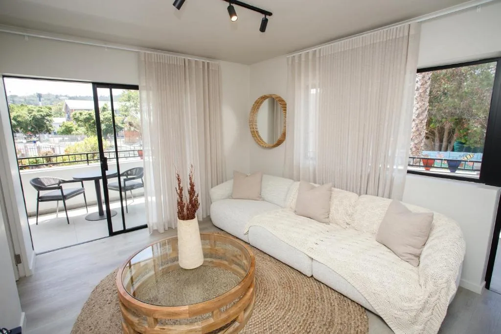 Bright lounge with cream sofa, round wooden table, and scenic water views from balcony