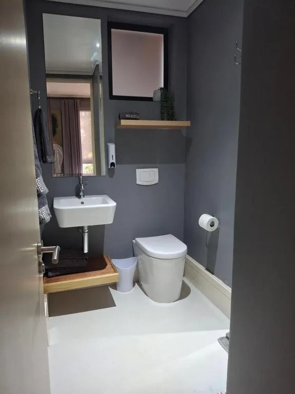 Modern bathroom with gray walls, white toilet, sink, and wooden shelf