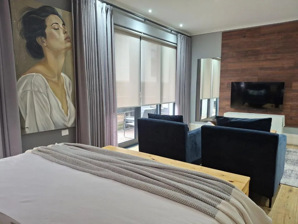 Modern bedroom with bed, artwork, black armchairs, and deck access