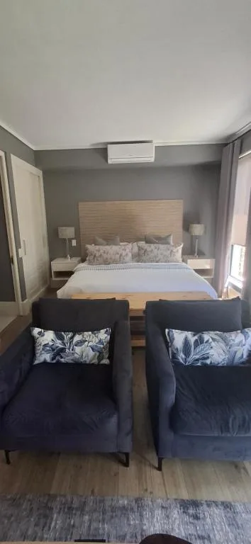 Modern bedroom with queen bed, grey walls, and two dark accent chairs