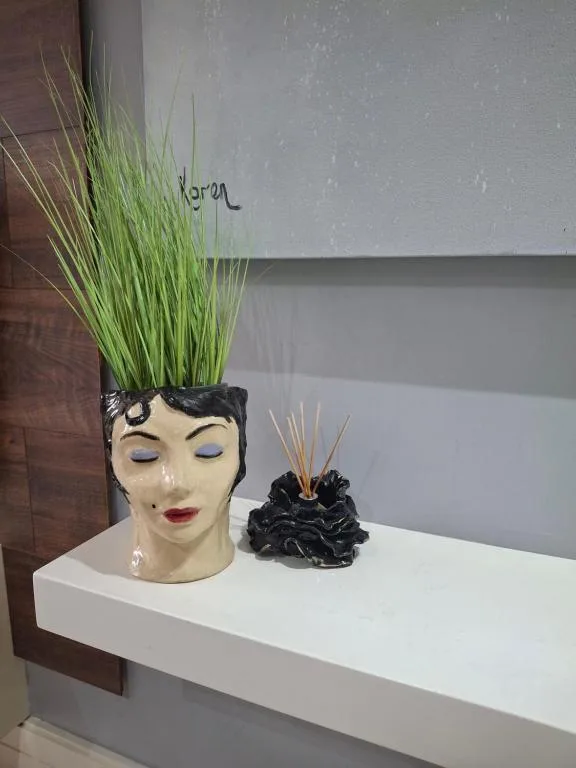 Decorative face planter with fresh green grass and artistic black vase on shelf