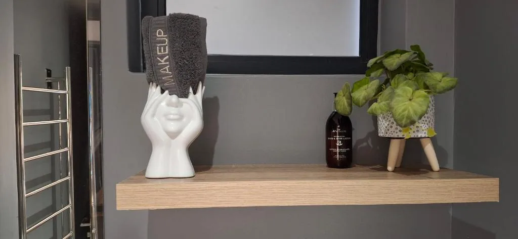 Bathroom shelf displaying hand towel, decorative head vase, potted plant, and toiletries