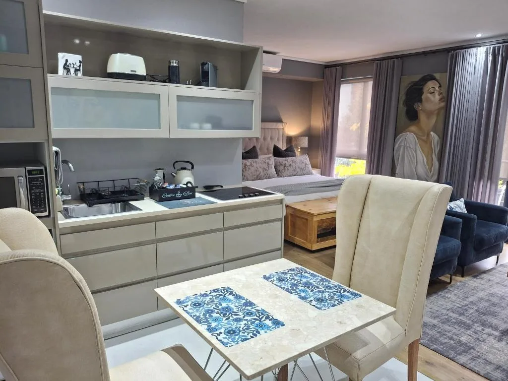 Open-plan lounge with cream dining chairs, modern kitchen, and bed visible beyond