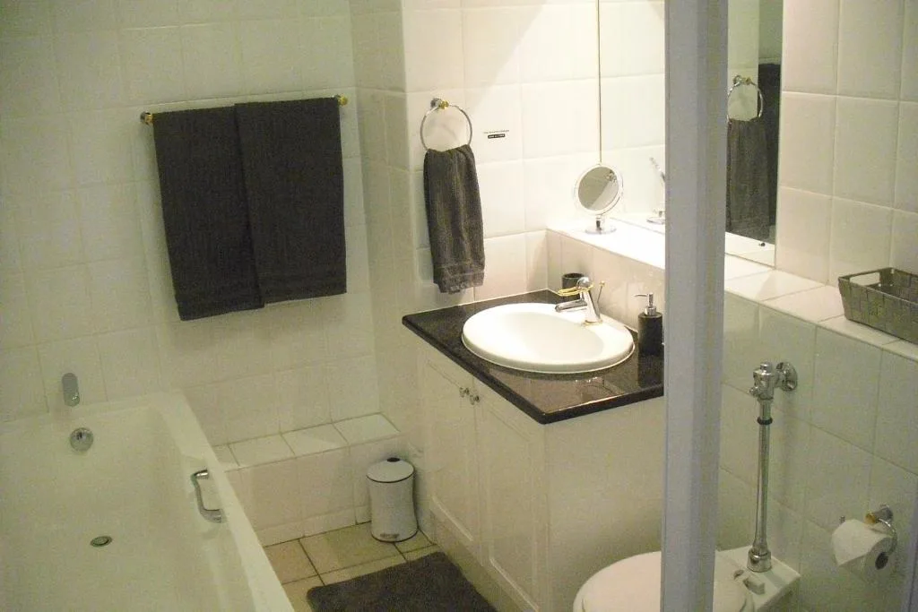 Clean bathroom with round sink, toilet, bathtub, and dark towels