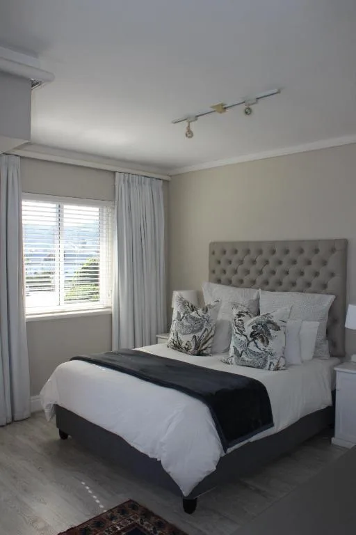 Modern bedroom with upholstered headboard, white bedding, patterned pillows and garden views