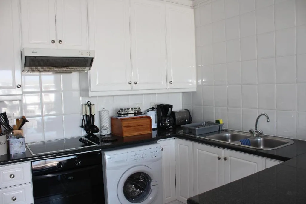 White kitchen with black countertops, oven, washing machine, and sink