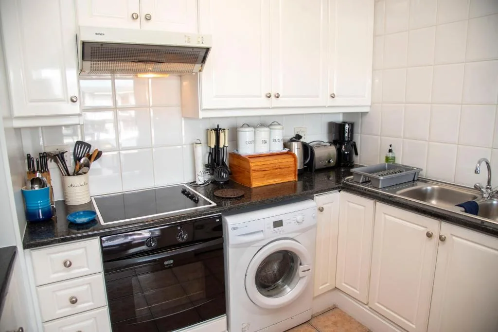 Modern white kitchen with black countertop, stove, washing machine, and sink