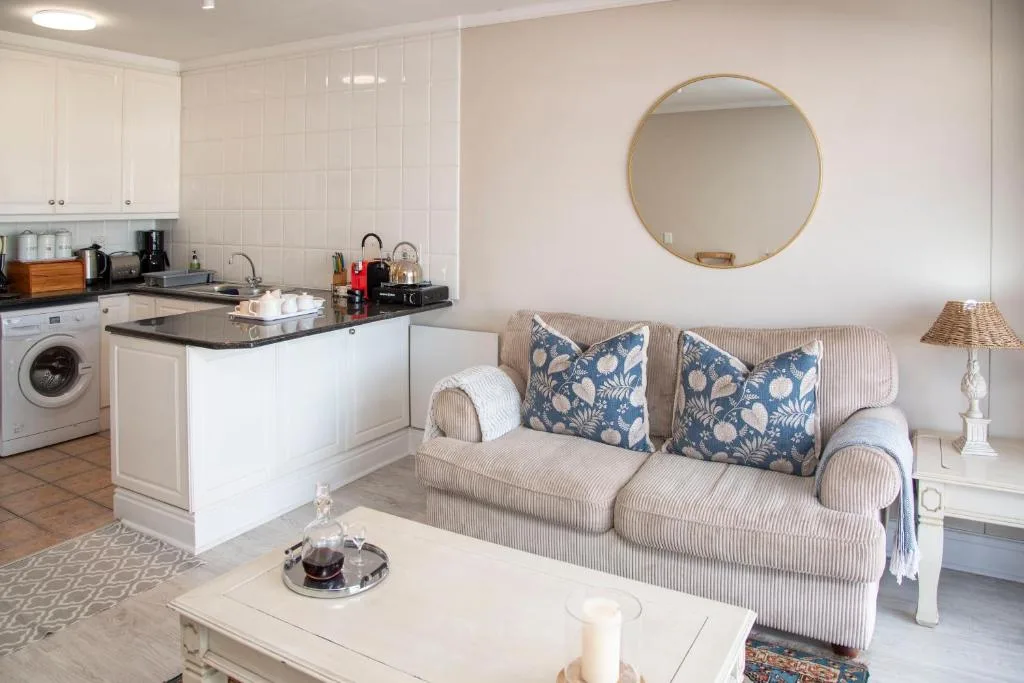 Open-plan lounge with striped sofa, decorative pillows, round mirror, and integrated kitchen