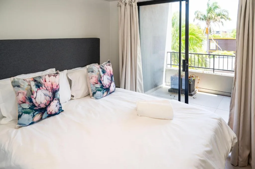Spacious bedroom with white linens, floral pillows, and balcony views of palm trees