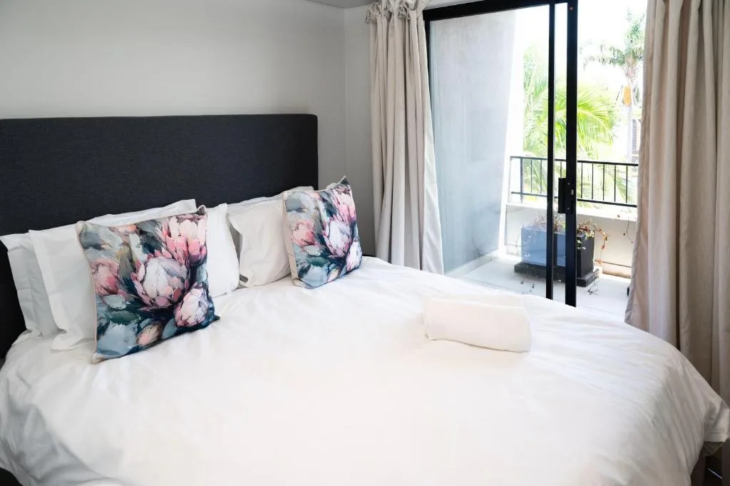 Bright bedroom with floral cushions, white linens, and garden view doors