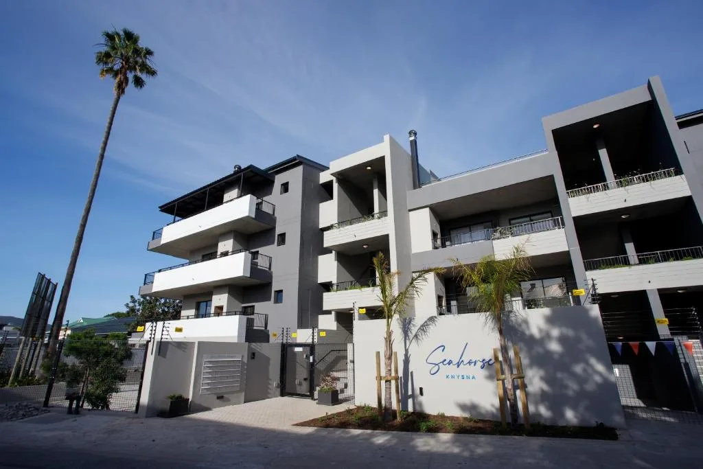 Modern white apartment building with multiple balconies and palm tree entrance