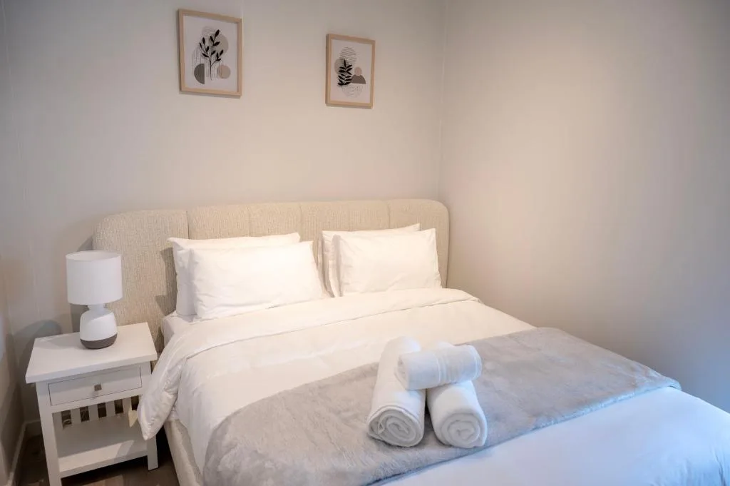 Bright bedroom with cream bedding, white pillows, and rolled towels on bed