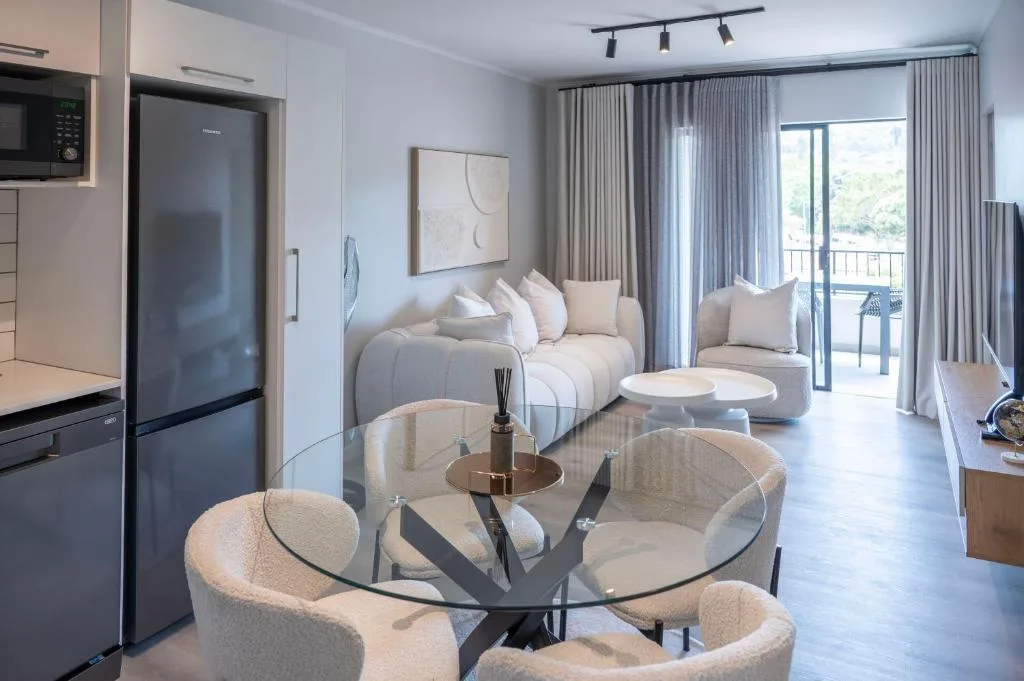Modern lounge with cream seating, glass dining table, kitchen visible