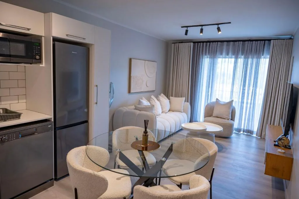 Modern lounge with cream seating, glass table, and open kitchen area