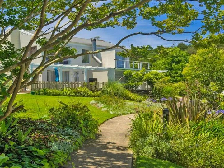 Modern home with manicured gardens, white picket fence, and mature trees
