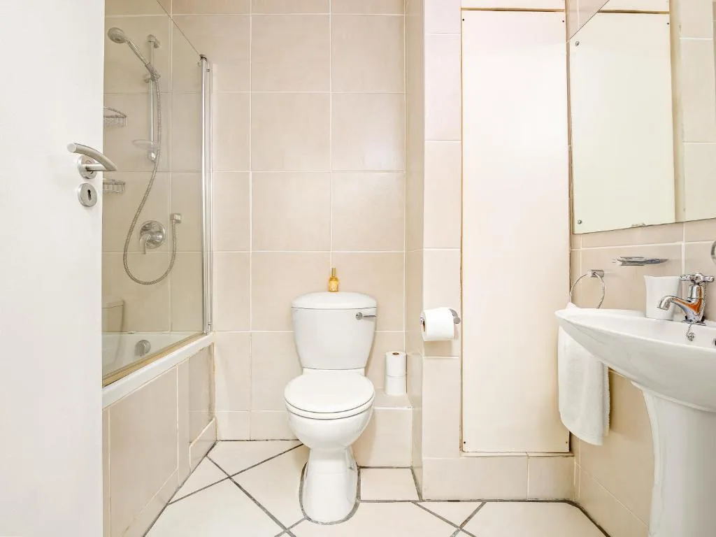 Clean bathroom with shower, toilet, sink and cream tile walls