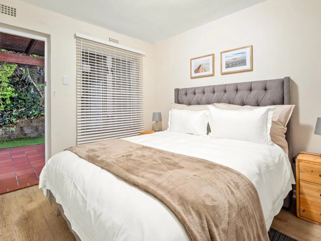 Bright bedroom with queen bed, gray upholstered headboard, garden access door