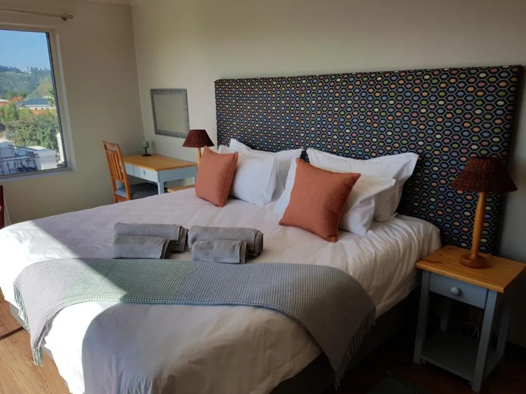 Bright bedroom with double bed, patterned headboard, and mountain views