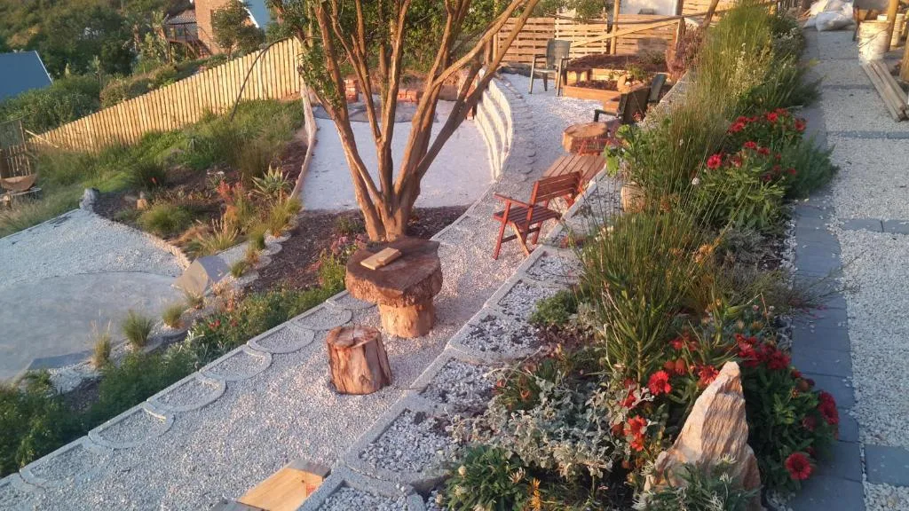 Garden patio with gravel pathways, native plants, wooden chairs and seating area