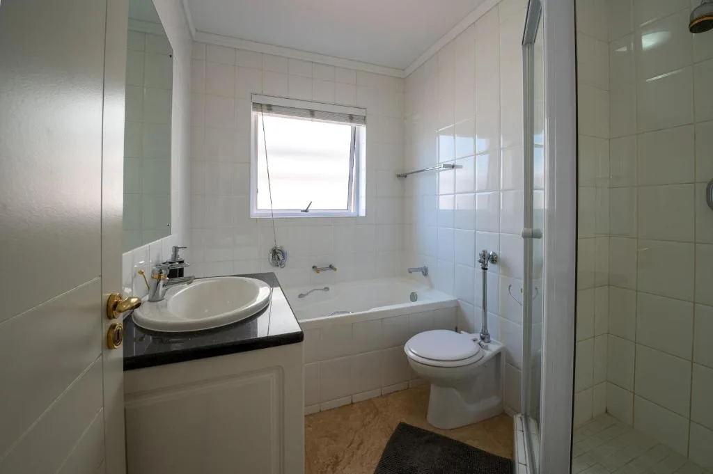 Modern bathroom with round sink, bathtub, toilet, and glass shower enclosure